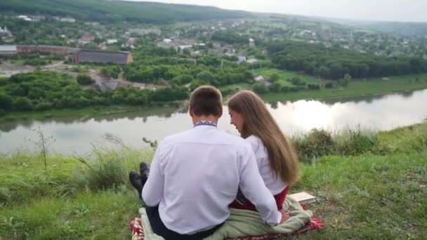 夫婦は丘の上に座っている 家族は公園に座っている自分の写真アルバムを見ています 写真アルバムと幸せなカップル 笑ったり話したりします 高品質のフルHd映像 — ストック動画