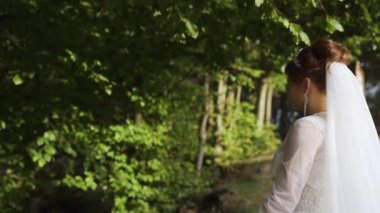 You bride fixing her hair in sunny park, back view. High quality FullHD footage