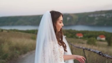 Fashion model posing. Fantasy woman queen in luxury long white dress stands outdoor by lake in sunset. Summer nature, water, river green trees. Girl princess beauty river nymph. 