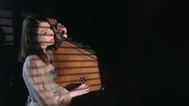 Bandura. Young beautiful woman plays on ukrainian musical instrument bandura. Dark room and light from the louver. High quality 4k footage