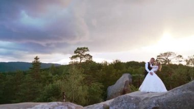 bride and groom standing on a cliff at sunset, blue clouds in the background. High-quality FullHD footage