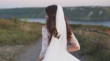 A bride in a wedding dress runs off into the distance on a dirt road, the view from the back is slow-motion. High quality FullHD footage