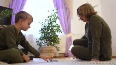 Little fun boy, grandson is sitting on the floor with his grandmother and plays with her, clapping his hands. Family weekend communication of generations. High quality 4k footage