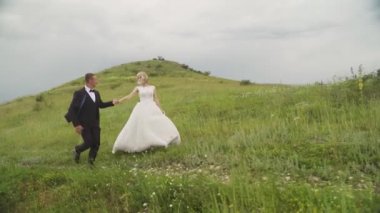 Happy young couple holding hands run through a wide field, having fun outdoors. Countryside. Man and woman running on the meadow. Happy joyful family outdoor. Slow motion High quality FullHD footage