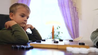 Happy little boy playing checkers with senior woman at home. Family relationship with grandmother and grandson. Grandma and male grandchild with board game. High quality 4k footage