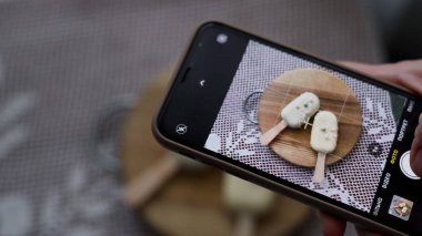 Sosyal medyada fotoğraf paylaşmak için elinde akıllı telefonuyla tatlı cheesecake 'in fotoğraflarını çeken bir kadın. Lezzetli kekten zevk alan çekici genç bir kız. 4k görüntü