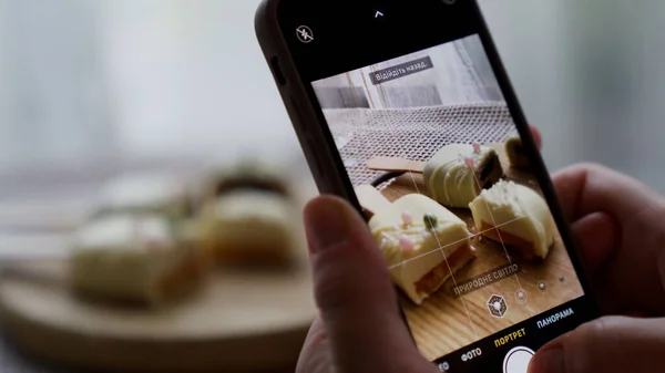 Sosyal medyada fotoğraf paylaşmak için elinde akıllı telefonuyla tatlı cheesecake 'in fotoğraflarını çeken bir kadın. Lezzetli kekten zevk alan çekici genç bir kız. 4k görüntü
