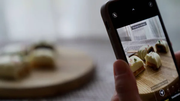 Sosyal medyada fotoğraf paylaşmak için elinde akıllı telefonuyla tatlı cheesecake 'in fotoğraflarını çeken bir kadın. Lezzetli kekten zevk alan çekici genç bir kız. 4k görüntü