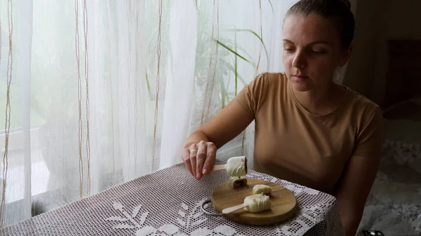 Evde tatlı yiyen bir kızın portresi. Elinde süslü pastayla tatmin olmuş bir kadın. Ev mutfağında ahşap tabaktan cheesecake yiyen çekici esmer kız. Yüksek kalite 4k görüntü