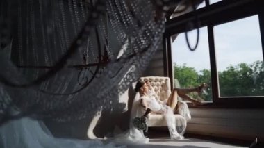 Koltuğunda dinlenen gülümseyen kadın düğün buketi ile hafifçe kendine dokunuyor. Kadın güzelliği, romantik ruh hali, evde çiçekler. Steadycam çekimi. Yüksek kaliteli FullHD görüntüler