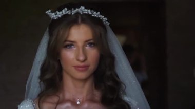 Beyaz perdelerle kameraya poz veren uzun kıvırcık saçlı, pullu gelinlik giyen zarif beyaz gelinin portresi. Yüksek kaliteli FullHD görüntüler