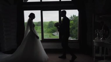 Pencerenin arkasında siluet var. Yeni evliler profil oluşturarak pencerede duruyorlar. Gelin ve damat parlak bir pencerenin yanında. Pencerenin yanındaki romantik çift silueti. Yüksek kaliteli FullHD görüntüler