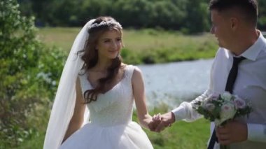 Mutlu yeni evliler, gülümsüyor ve nehir kıyısında yürüyorlar. Steadycam çekimi. Yüksek kaliteli FullHD görüntüler