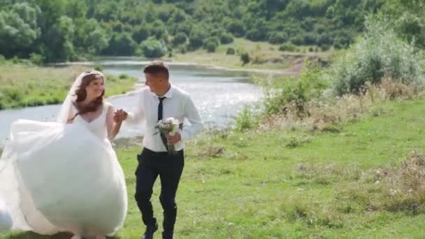 結婚式のカップル山の川の近くを実行している 新郎は花嫁の手を握って回転します 幸せな家族だ 定常カム撮影 高品質のフルHd映像 — ストック動画