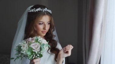 Beyaz perdelerle kameraya poz veren uzun kıvırcık saçlı, pullu gelinlik giyen zarif beyaz gelinin portresi. Yüksek kaliteli FullHD görüntüler