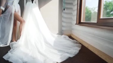 İpek Giysili Gelinlik Tutuyor ve pencerenin yanındaki güzel gelinliğine hayran. Yüksek kaliteli FullHD görüntüler