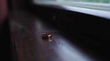 İki altın alyansın yakın plan çekimi. Gelin halkaları ahşap masada ağır çekimde döner. Yüksek kaliteli FullHD görüntüler