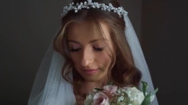 Beyaz perdelerle kameraya poz veren uzun kıvırcık saçlı, pullu gelinlik giyen zarif beyaz gelinin portresi. Yüksek kaliteli FullHD görüntüler