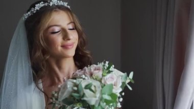 Beyaz perdelerle kameraya poz veren uzun kıvırcık saçlı, pullu gelinlik giyen zarif beyaz gelinin portresi. Yüksek kaliteli FullHD görüntüler