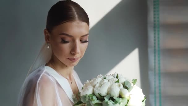 結婚式の日の朝 ぶら下がっているウェディングドレスの近くにポーズをとるエレガントな花嫁 高品質のフルHd映像 — ストック動画