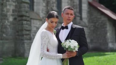 Yeni evlilerin portresi. Güzel Kafkas gelini, damat eski kalenin yanında yürüyor. Sarılmak, sarılmak, öpüşmek. Mutlu evlilik çifti ailesi. Aşık bir erkek. Gelinlik giymiş gelin. Yüksek kalite FullHD