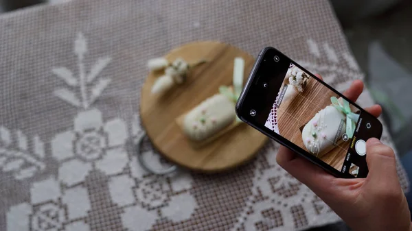 Sosyal medyada fotoğraf paylaşmak için elinde akıllı telefonuyla tatlı cheesecake 'in fotoğraflarını çeken bir kadın. Lezzetli kekten zevk alan çekici genç bir kız. 4k görüntü