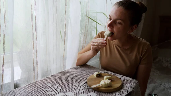 Evde tatlı yiyen bir kızın portresi. Elinde süslü pastayla tatmin olmuş bir kadın. Ev mutfağında ahşap tabaktan cheesecake yiyen çekici esmer kız. Yüksek kalite 4k görüntü