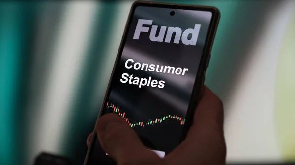 一个投资者正在屏幕上分析消费主食等基金 一部电话显示了消费品主要股票的价格 — 图库照片
