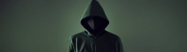 Yeşil kapüşonlu, yeşil arka planda, isimsiz bir hacker. Siber korsan yüzü izole edilmiş stüdyo ön planı, metin için boşluk.