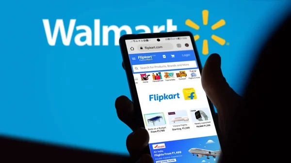 stock image July 31th, someone holds a phone on the site of Flipkart, in the background a part of blurry logo of Wallmart.