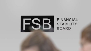 FSB Mali İstikrar Kurulu logosu beyaz bir duvarda, önplanda yoldan geçenlerin iki bulanık silueti.