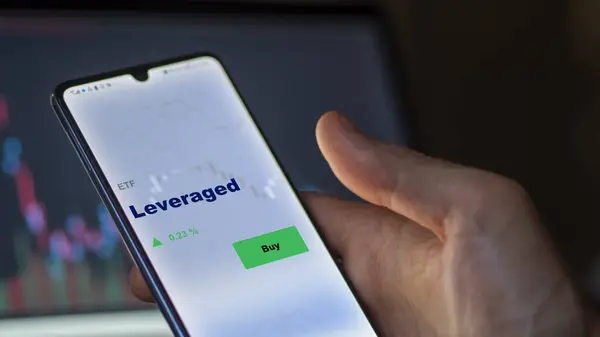 stock image An investor analyzing the leveraged etf fund on a screen. A phone shows the prices of Leveraged