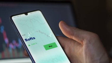 Bir yatırımcı ekrandaki yumuşak etf fonunu analiz ediyor. Bir telefon Softs 'ın fiyatlarını gösterir