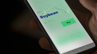 Ekranda soya fasulyesi fonunu analiz eden bir yatırımcı. Bir telefon soya fasulyesinin fiyatlarını gösteriyor.