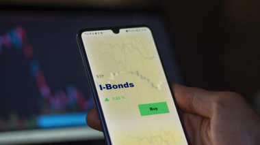 Ekrandaki i-bonoları analiz eden bir yatırımcı. Bir telefon I-Bonds fiyatlarını gösterir
