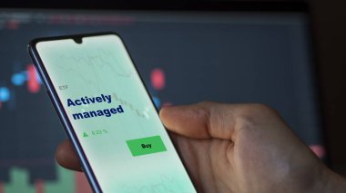 Aktif olarak yönetilen etf fonunu ekranda analiz eden bir yatırımcı. Bir telefon aktif olarak yönetilen fiyatları gösterir