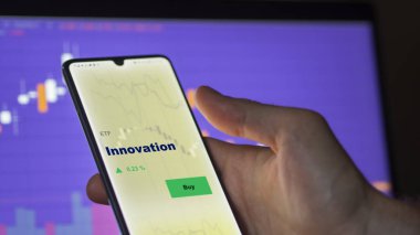 Bir yatırımcı ekrandaki yenilikçi ETF fonunu analiz ediyor. Bir telefon İnovasyon fiyatlarını gösterir