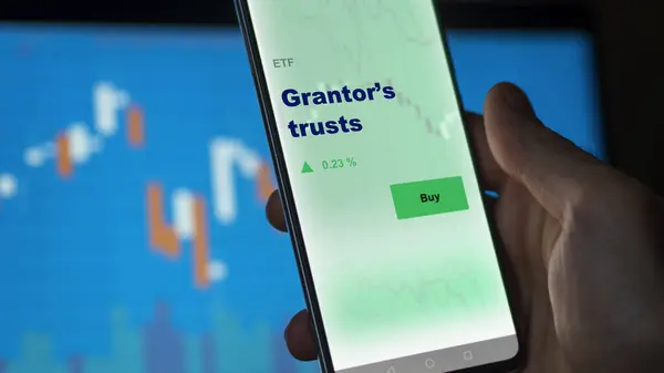 stock image An investor analyzing the grantor s trusts etf fund on a screen. A phone shows the prices of Grantors trusts