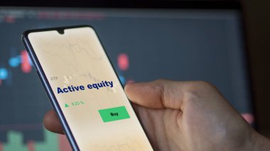 Ekrandaki aktif sermaye fonunu analiz eden bir yatırımcı. Bir telefon aktif sermaye fiyatlarını gösterir