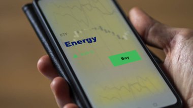 Ekrandaki enerji fonunu analiz eden bir yatırımcı. Bir telefon enerji fiyatlarını gösterir