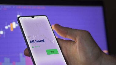 Ekrandaki tüm tahvil fonlarını analiz eden bir yatırımcı. Bir telefon tüm tahvillerin fiyatlarını gösterir