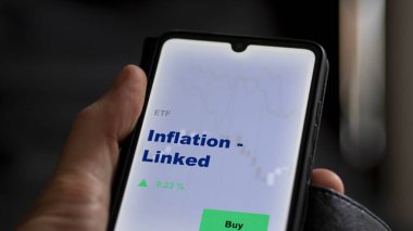 Enflasyonu analiz eden bir yatırımcı. Ekrandaki etf fonu ile bağlantılı. Bir telefon enflasyon fiyatlarını gösterir - bağlantılı
