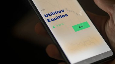 Bir yatırımcı ekrandaki kamu hizmetleri sermaye fonunu analiz ediyor. Bir telefon kamu hizmetleri varlıklarının fiyatlarını gösterir