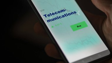 Telekomünikasyon fonunu ekranda analiz eden bir yatırımcı. Telekomünikasyon fiyatlarını gösteren bir telefon