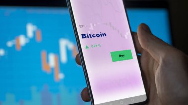 Ekranda Bitcoin etf fonunu analiz eden bir yatırımcı. Bitcoin 'in fiyatlarını gösteren bir telefon