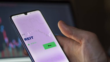 Ekrandaki Reit ETF fonunu analiz eden bir yatırımcı. REIT 'in fiyatlarını gösteren bir telefon