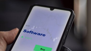 Yazılım fonunu ekranda analiz eden bir yatırımcı. Bir telefon yazılım fiyatlarını gösterir