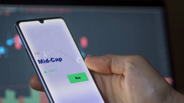 An investor analyzing the mid-cap etf fund on a screen. A phone shows the prices of middle capitalization