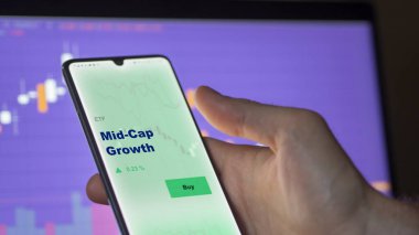 Bir yatırımcı ekrandaki orta kapasite büyüme etf fonunu analiz ediyor. Bir telefon Mid-Cap Büyümesinin fiyatlarını gösterir