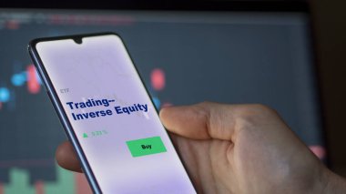 An investor analyzing the trading-inverse equity etf fund on a screen. A phone shows the prices of trading inverse equities